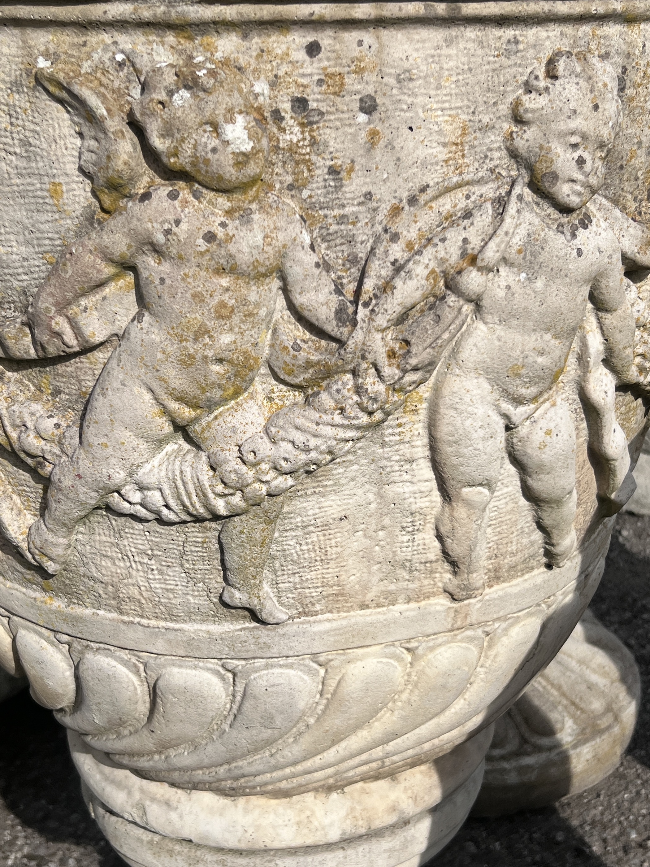 A pair of large circular reconstituted stone garden planters, moulded with a band of putti on square bases, diameter 53cm, height 89cm
